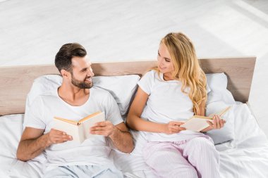 evde kitap ile yatakta yatan güzel gülümseyen çift 
