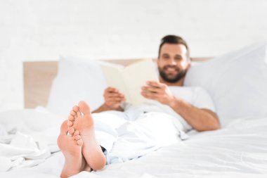 smiling man lying in bed and reading book in morning clipart