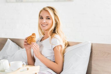 kahvaltı sırasında yatakta evde kruvasan tutan güzel mutlu kadın