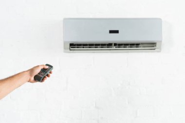 cropped view of man suffering from heat and switching temperature of air conditioner at home clipart