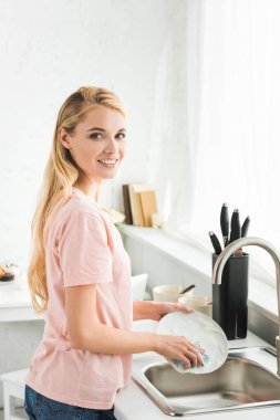 beautiful happy woman washing dishes at kitchen in morning clipart