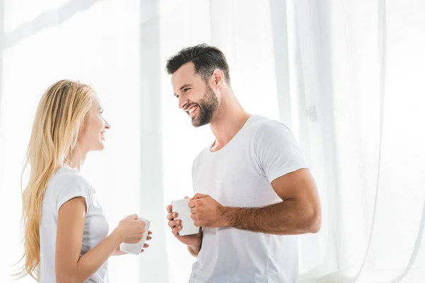 美丽的夫妇与咖啡杯看着对方在家里在早上 — 图库照片