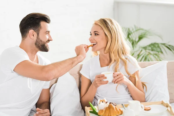 朝ベッドで朝食を食べるパジャマの美しいカップル — ストック写真