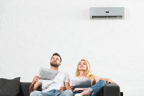 自宅のエアコンの下で熱に苦しむ新聞とソファのカップル — ストック写真
