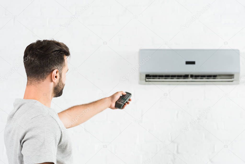 side view of man suffering from heat and switching temperature of air conditioner at home