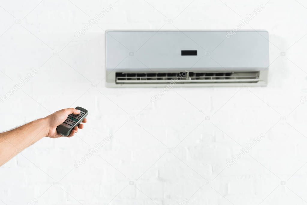cropped view of man suffering from heat and switching temperature of air conditioner at home