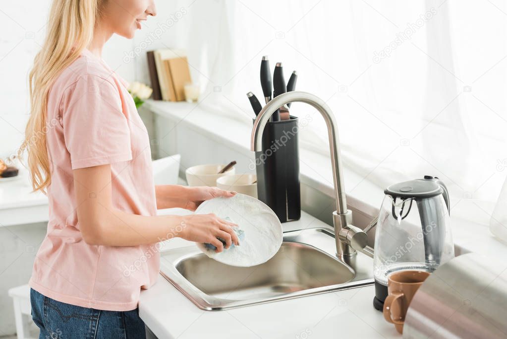 cropped view of woman washing dishes at kitchen in morning