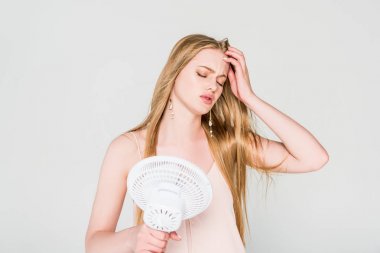 young woman suffering from heat and holding Electric Fan isolated on grey clipart