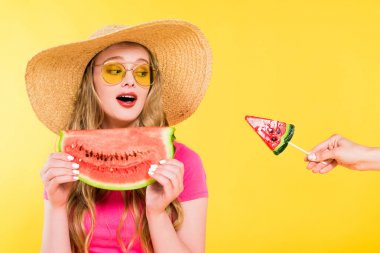 beautiful surprised girl in Straw Hat with watermelon looking at lollipop Isolated On yellow  clipart