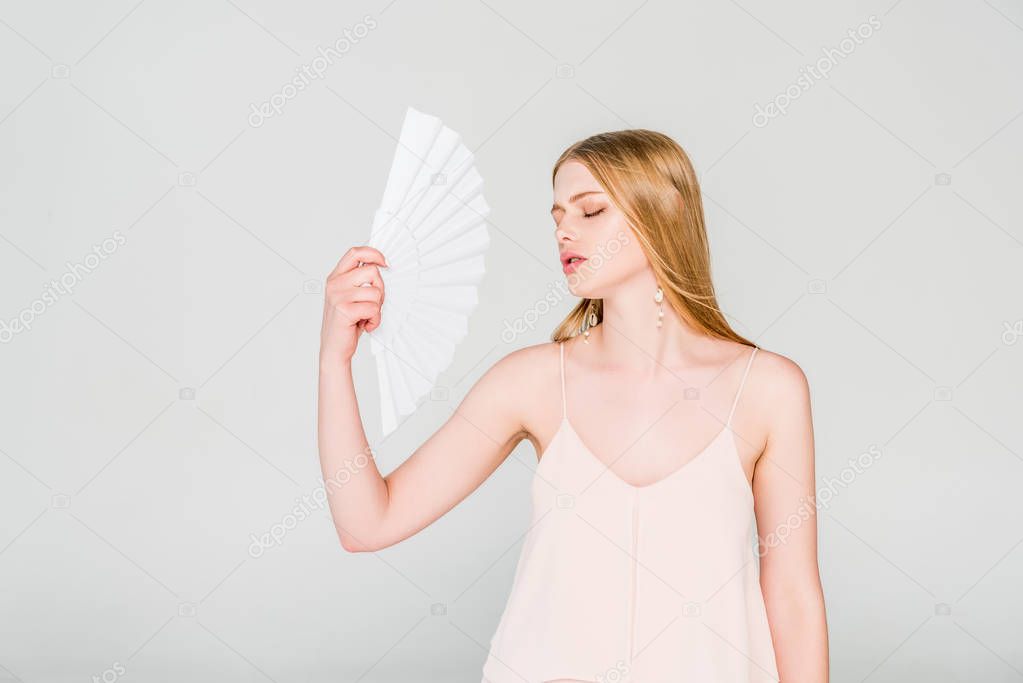 beautiful young woman with hand fan suffering from heat on grey