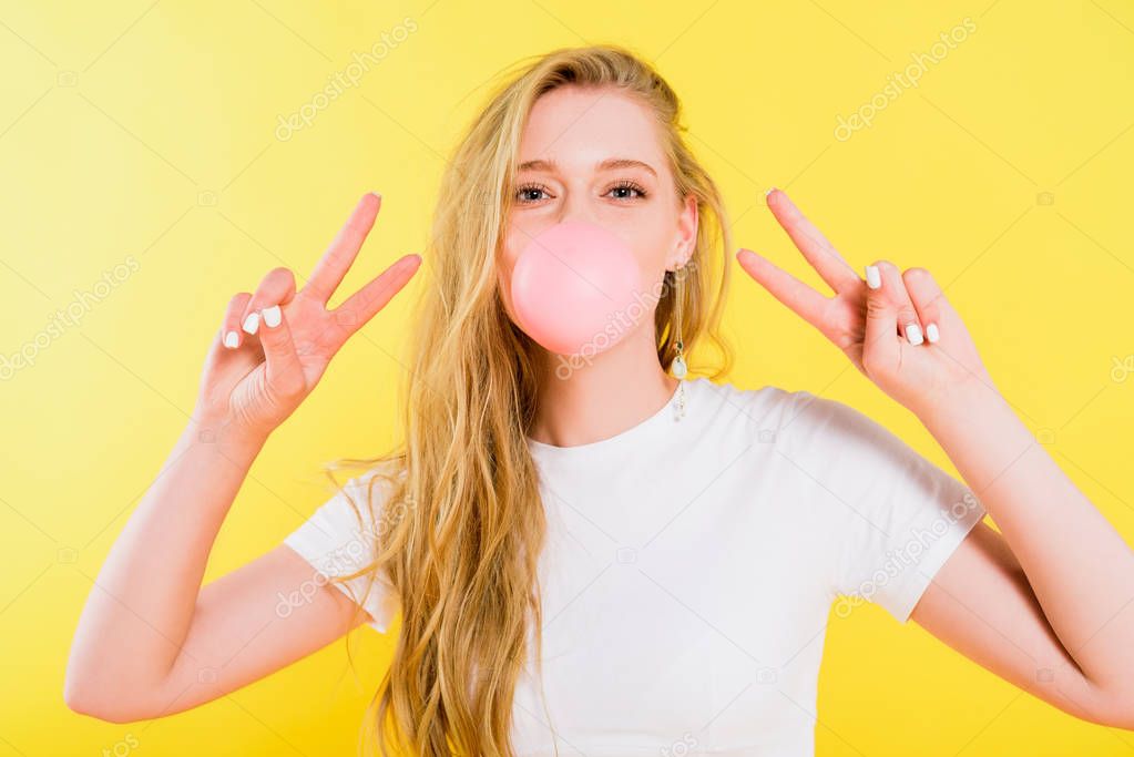 beautiful girl blowing bubble gum and doing peace signs Isolated On yellow