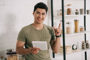 neşeli Asya adam dijital tablet tutarak ve kamera gülümsüyor sırasında fikir işareti gösteren