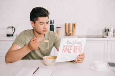 Mutfakta sahte haber gazetesi okurken yakışıklı Asya adam kahvaltı