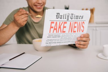 Mutfakta sahte haber gazetesi okurken gevreği yeme gülümseyen adam kırpılmış görünümü