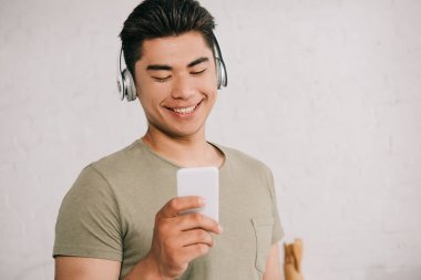 akıllı telefonda bakarken neşeli Asya adam kulaklıkta müzik dinleme