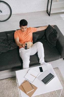 Genç Asya adam yüksek açı görünümü Popcorn kase ile kanepede oturan ve TV izlerken