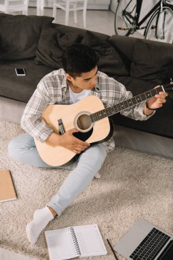evde kanepede oturan ve akustik gitar oynarken Genç Asyalı adam
