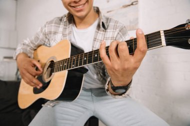 evde akustik gitar oynarken gülümseyen genç adamın kısmi görünümü