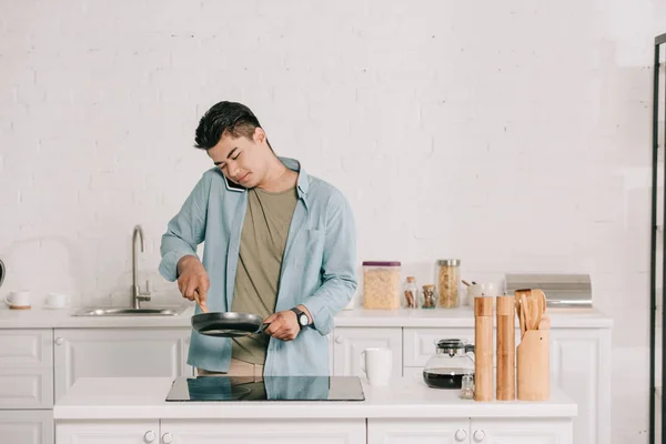 Handsome Asian Man Preparing Breakfast Frying Pan While Talking Smartphone — Stock Photo, Image