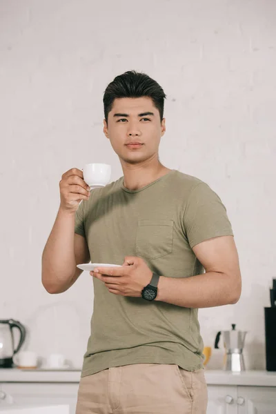 Zamyślony Asian Mężczyzna Picie Kawy Stojąc Kuchni Patrząc Dala — Zdjęcie stockowe