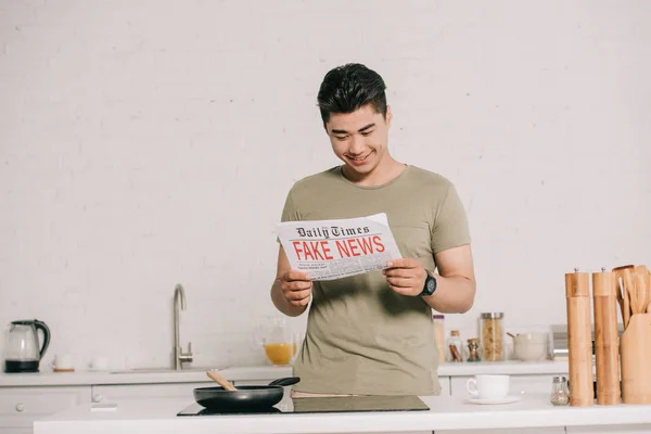 Sorrindo Asiático Homem Ler Falso Notícias Jornal Enquanto Perto Cozinhar — Fotografia de Stock