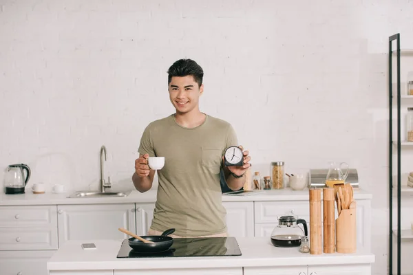 Vrolijke Aziatische Man Die Koffie Kopje Wekker Houdt Terwijl Hij — Stockfoto