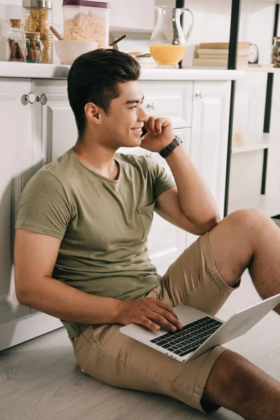 Sorrindo Asiático Homem Falando Smartphone Usando Laptop Enquanto Sentado Chão — Fotografia de Stock