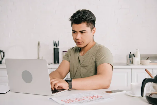 台所のテーブルに座っている間 ラップトップを使用して若い 気配りのアジアの男性 — ストック写真