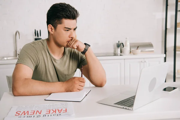 Serious Asian Man Looking Laptop Holding Pencil While Sitting Kitchen — Stock Photo, Image