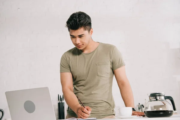 Красивый Азиатский Мужчина Смотрит Ноутбук Стоя Возле Кухонного Стола — стоковое фото