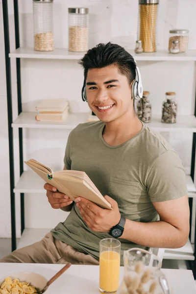 Alegre Asiático Hombre Auriculares Sonriendo Cámara Mientras Sentado Cocina Mesa — Foto de Stock