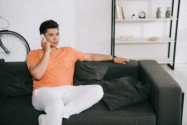 Serious Asian Man Talking Smartphone Looking Away While Sitting Sofa — Stock Photo, Image