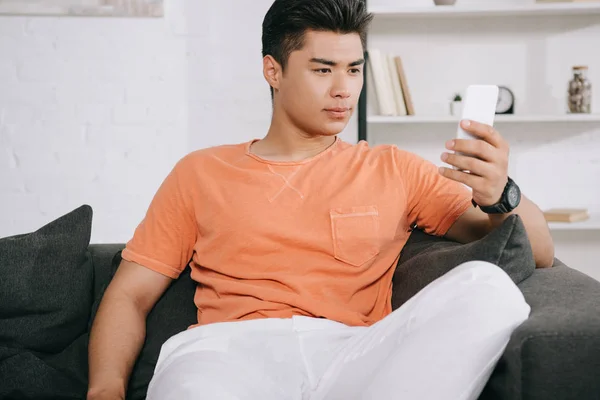 Serious Asian Man Using Smartphone While Sitting Couch Home — Stock Photo, Image