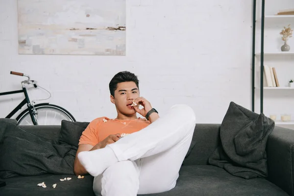 Young Asian Man Eating Popcorn Looking Camera While Sitting Sofa — Stock Photo, Image