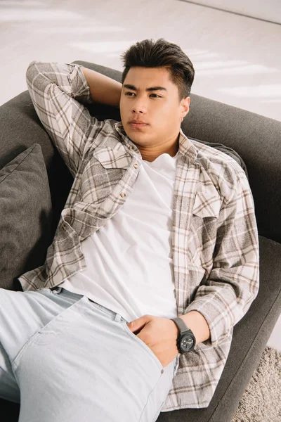 Young Dreamy Asian Man Looking Away While Lying Sofa Home — Stock Photo, Image