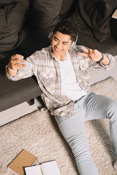 바닥에 앉아있는 셀카를 헤드폰에서 쾌활한 아시아 남자의 — 스톡 사진