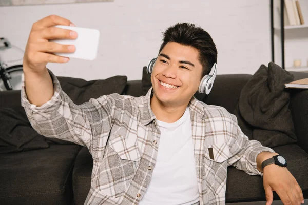 Cheerful Asian Man Headphones Taking Selfie Smartphone While Sitting Couch — Stock Photo, Image