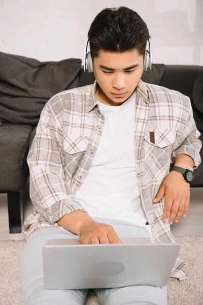 Attentive Asian Man Headphone Using Laptop While Sitting Floor Home — Stock Photo, Image