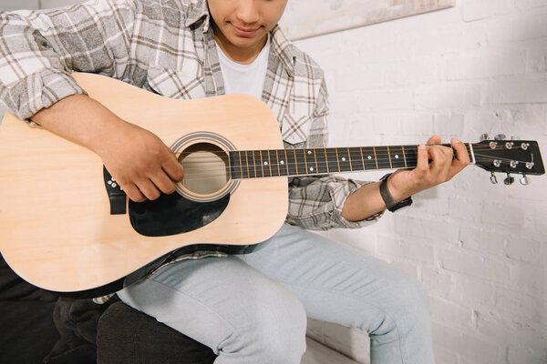 cropped view of young man playing acoustic guitar at home