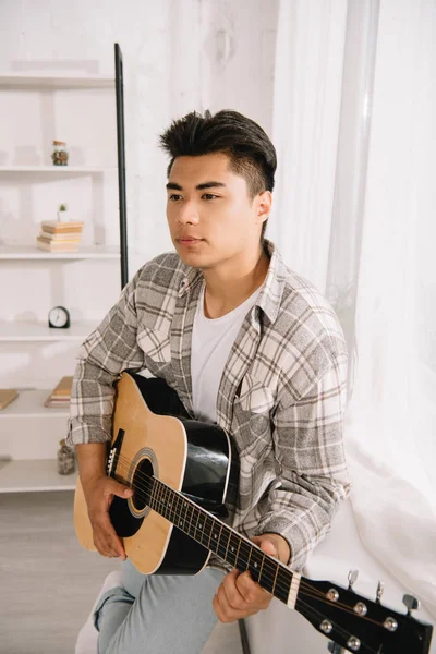 Nachdenklicher Asiate Schaut Weg Während Hause Akustikgitarre Spielt — Stockfoto