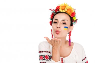 brunette young woman in national Ukrainian embroidered shirt and floral wreath blowing kiss isolated on white clipart