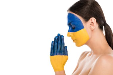 side view of naked young woman with painted Ukrainian flag on skin praying with closed eyes isolated on white clipart