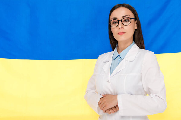 уверенный врач в белом халате на фоне украинского флага
