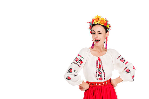 brunette young woman in national Ukrainian costume with hands on hips winking isolated on white