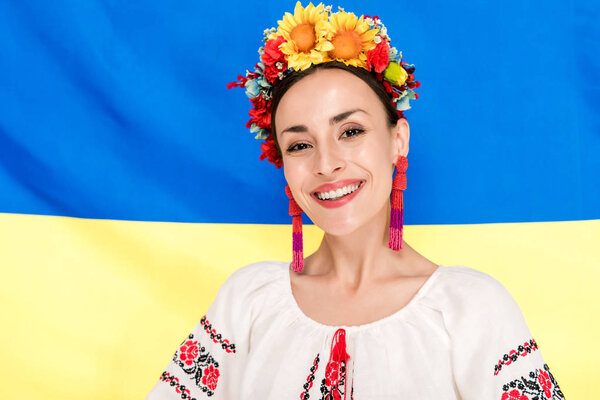 happy brunette young woman in national Ukrainian costume with flag of Ukraine on background