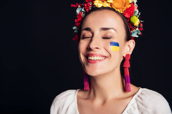 happy brunette young woman in national Ukrainian costume with closed eyes isolated on black