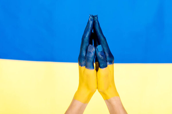 cropped view of painted praying hands on Ukrainian flag background