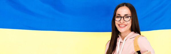smiling brunette young woman with backpack on Ukrainian flag background, panoramic shot