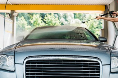 cropped view of cleaner standing and washing grey automobile outside clipart