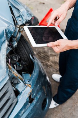 cropped view of man pointing with finger at digital tablet with blank screen near damaged car  clipart